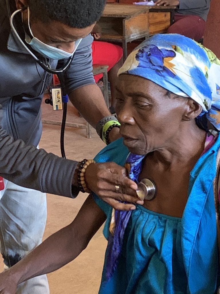 A health worker with a stethoscope examining an older woman.